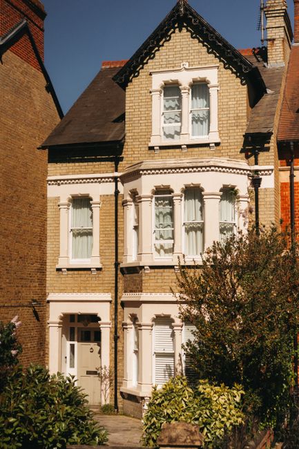 Exterior view of a row of white terraced houses in Abbeville Village, Clapham, with visible ground-floor garages, some painted in dark blue. The houses feature external staircases leading to upper-flo