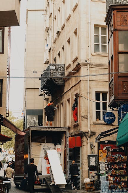 A moving team from Man and Van Clapham is engaged in a home relocation process on a busy urban street, with their vehicle parked directly adjacent to an older, multi-storey building with cream-colored