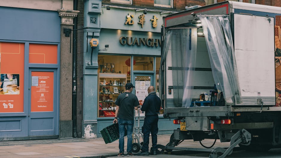 A moving team from Man and Van Clapham is engaged in a home relocation process on a busy urban street, with their vehicle parked directly adjacent to an older, multi-storey building with cream-colored